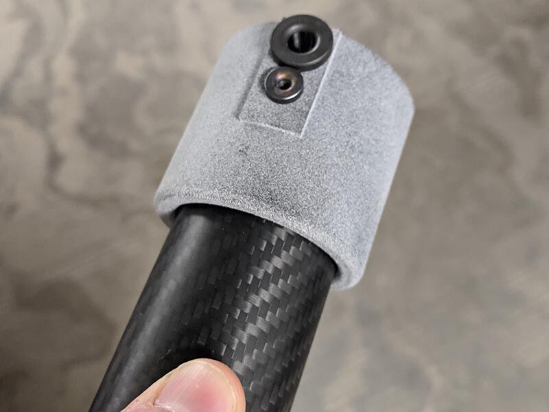 The custom assembly, a metallic grey fixture with two circular inserts, bonded to the end of a carbon fiber tube.
